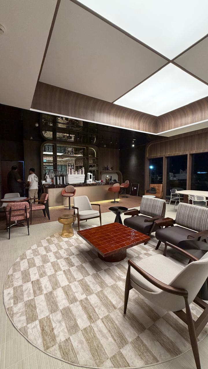 Lounge chairs on a round rug in front of the arched bar, under backlit ceiling panels