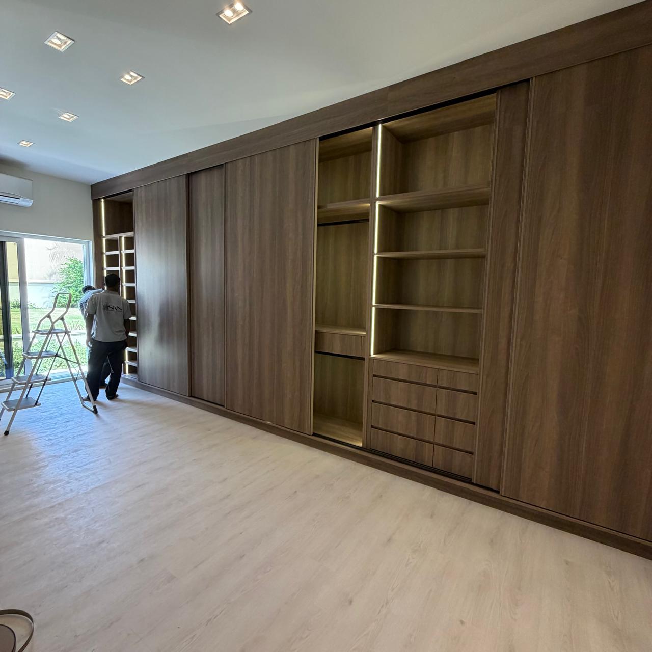 Wall of full-height timber wardrobes with lit open shelving